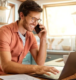 Man smiling at laptop while on the phone