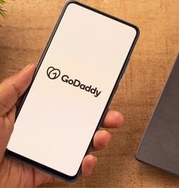 Hand holding a phone with the GoDaddy logo on the screen