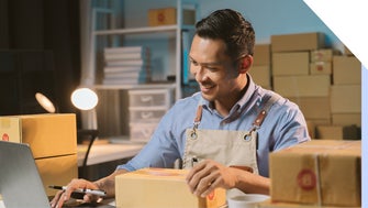 Man sits at desk smiling at laptop while boxing packages