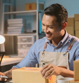 Man sits at desk smiling at laptop while boxing packages