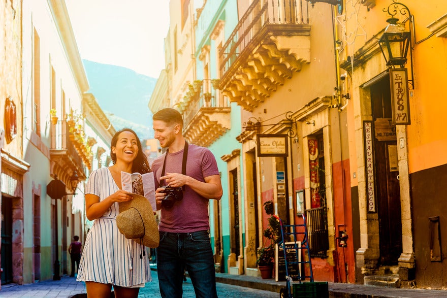 Jim and May smiling on a pretty street holding a map and camera