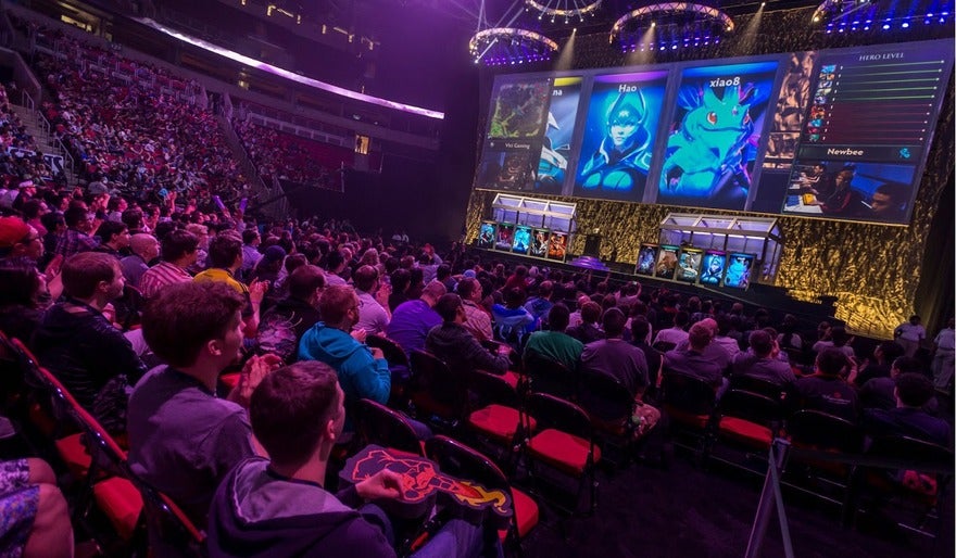 Esports Audience watching an esports tournament with large screens displaying video game characters and player profiles.