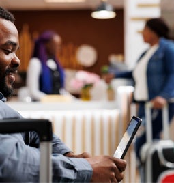 Male tourist sits with his suitcase looking at his tablet