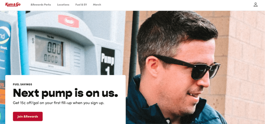 Kum & Go A man in sunglasses smiles at a fuel station next to a pump displaying zero cost, under a promotional sign offering fuel savings for new members.