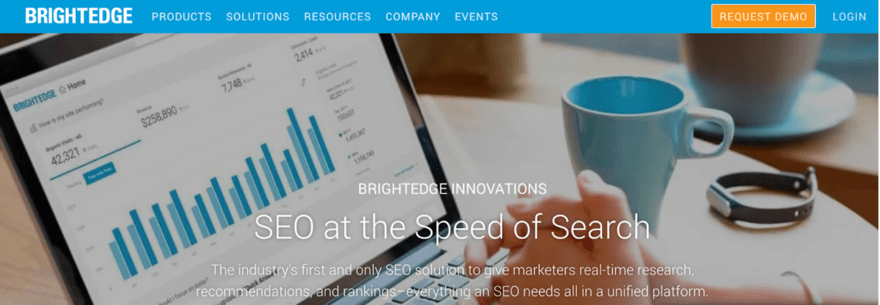 Brightedge The image shows a digital device displaying analytical data, with the heading "SEO at the Speed of Search". It suggests that the tool provides SEO solutions with real-time research, recommendations, and rankings. The setting includes a cup of coffee, indicating a work environment, possibly highlighting the ease and convenience of using the software for SEO tasks. The BrightEdge logo is prominent at the top, indicating the brand offering this service.