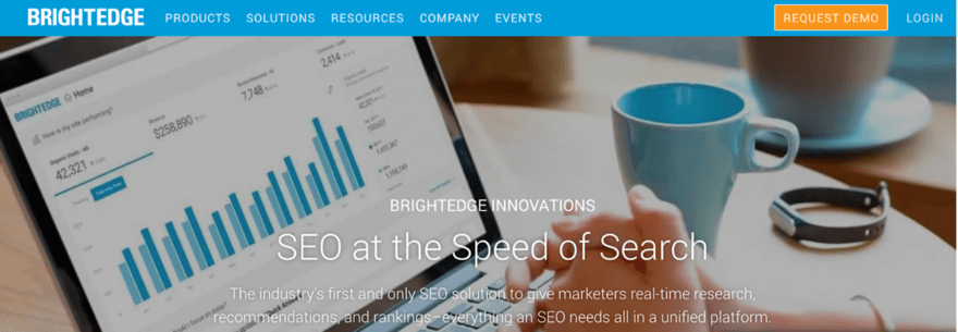 The image shows a digital device displaying analytical data, with the heading "SEO at the Speed of Search". It suggests that the tool provides SEO solutions with real-time research, recommendations, and rankings. The setting includes a cup of coffee, indicating a work environment, possibly highlighting the ease and convenience of using the software for SEO tasks. The BrightEdge logo is prominent at the top, indicating the brand offering this service.