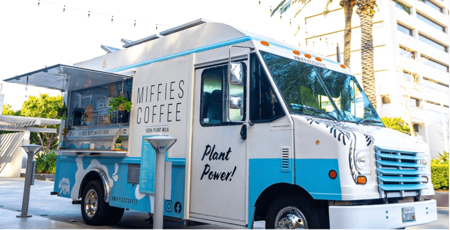 Miffies A white food truck named Miffie's Coffee is parked in front of a tall building. The truck sells 100% plant-based coffee and other drinks.