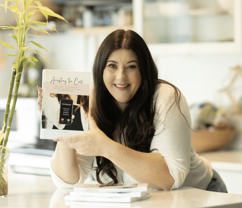 Screen Shot 2023-07-14 at 12.43.07 AM (1) a woman smiling holding a book in a soft-coloured kitchen
